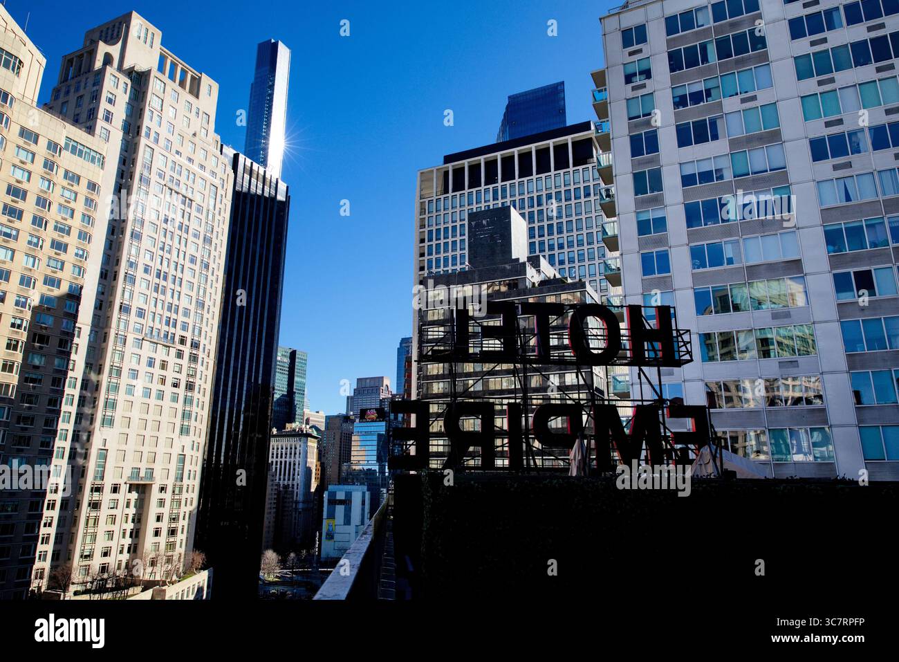Das ikonische Dachschild des Empire Hotels erhebt sich über dem Columbus Circle, hinter dem sich die Türme von Midtown Manhattan unter dem strahlend blauen Winterhimmel erheben. Stockfoto