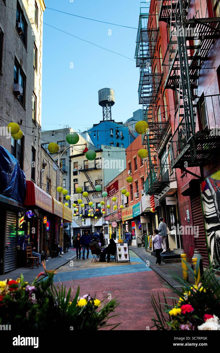 Die geschwungene Gasse der Doyers Street in Chinatown, Manhattan, ist mit Hängeleuchten, Feuerflüchten und einem lebhaften Straßenleben unter einem strahlend blauen Himmel geschmückt. Stockfoto