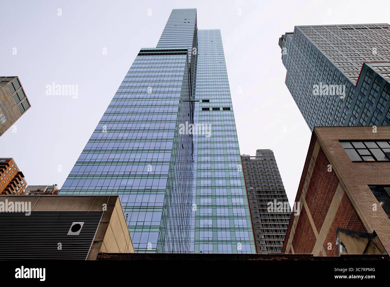 Schweben Sie unter einem glänzenden Glashochhaus auf Manhattans Skyline, wo reflektierende Paneele nach oben gegen einen klaren Himmel in der Stadt kaskadieren, um dramatische Effekte zu erzielen. Stockfoto