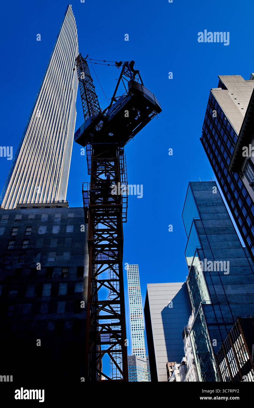 Ein Baukran steht im Schatten eines Vanderbilt Glasturms auf einer Midtown Manhattan Street und unterstreicht die vertikale Energie der Stadt. Stockfoto