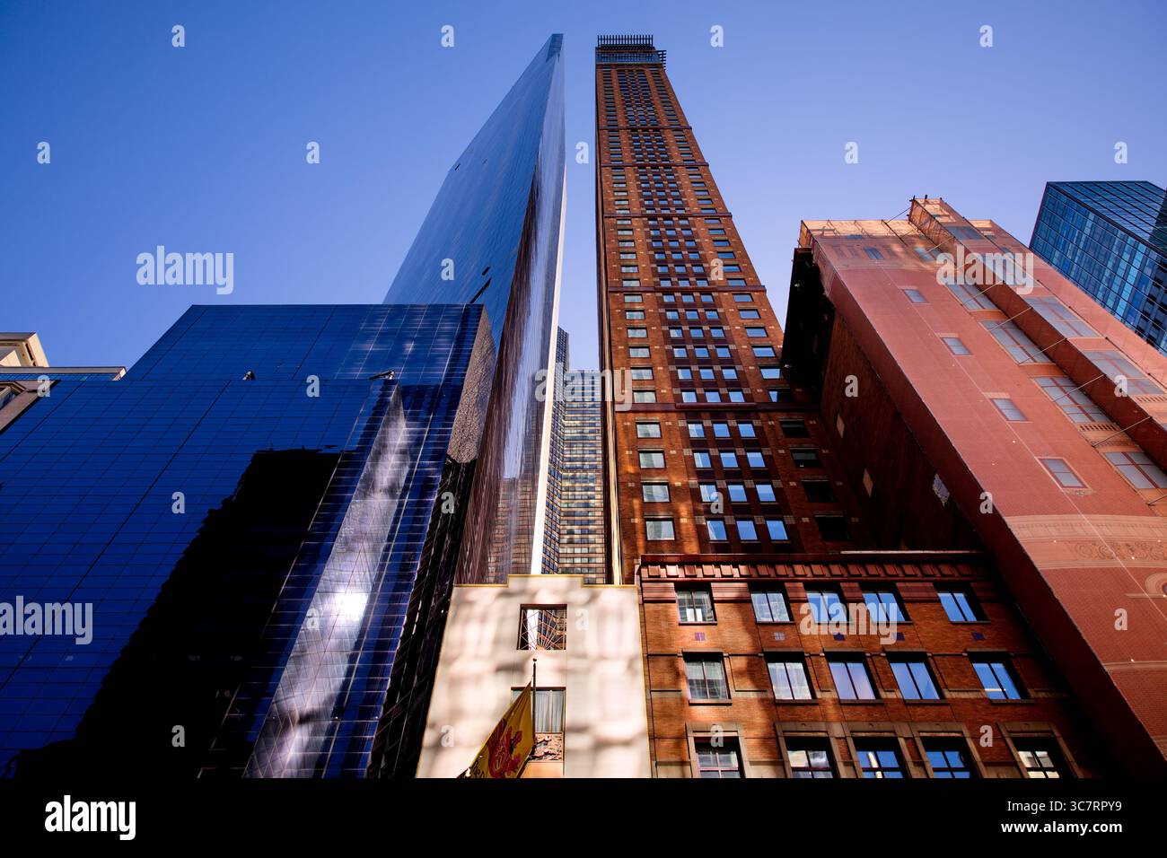 Ein Vanderbilt-Glasturm und ein Backsteinhochhaus ragen über Midtown Manhattan in einer Niedrigwinkelaufnahme auf, die Alt und Neu im Kontrast zu einem klaren Himmel stellt. Stockfoto