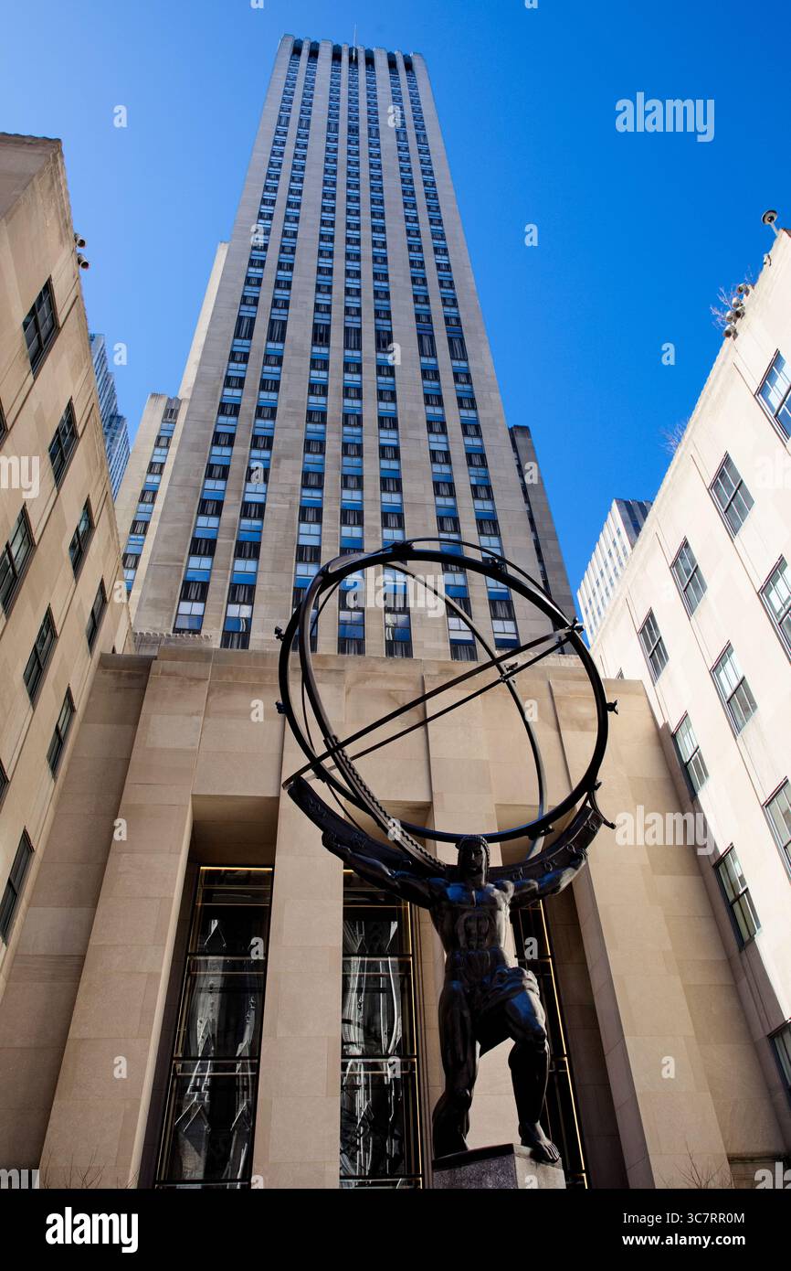 Die Atlas-Statue im Rockefeller Center steht unter dem hoch aufragenden Art déco-Turm des Rockefeller Plaza 30, der von flankierenden Flügeln unter einem klaren blauen Himmel eingerahmt wird. Stockfoto