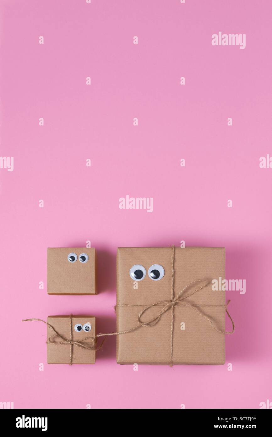 Karte mit braunen Geschenkboxen mit Augen auf rosa Hintergrund. Platz für Ihren Text, vertikal. Stockfoto
