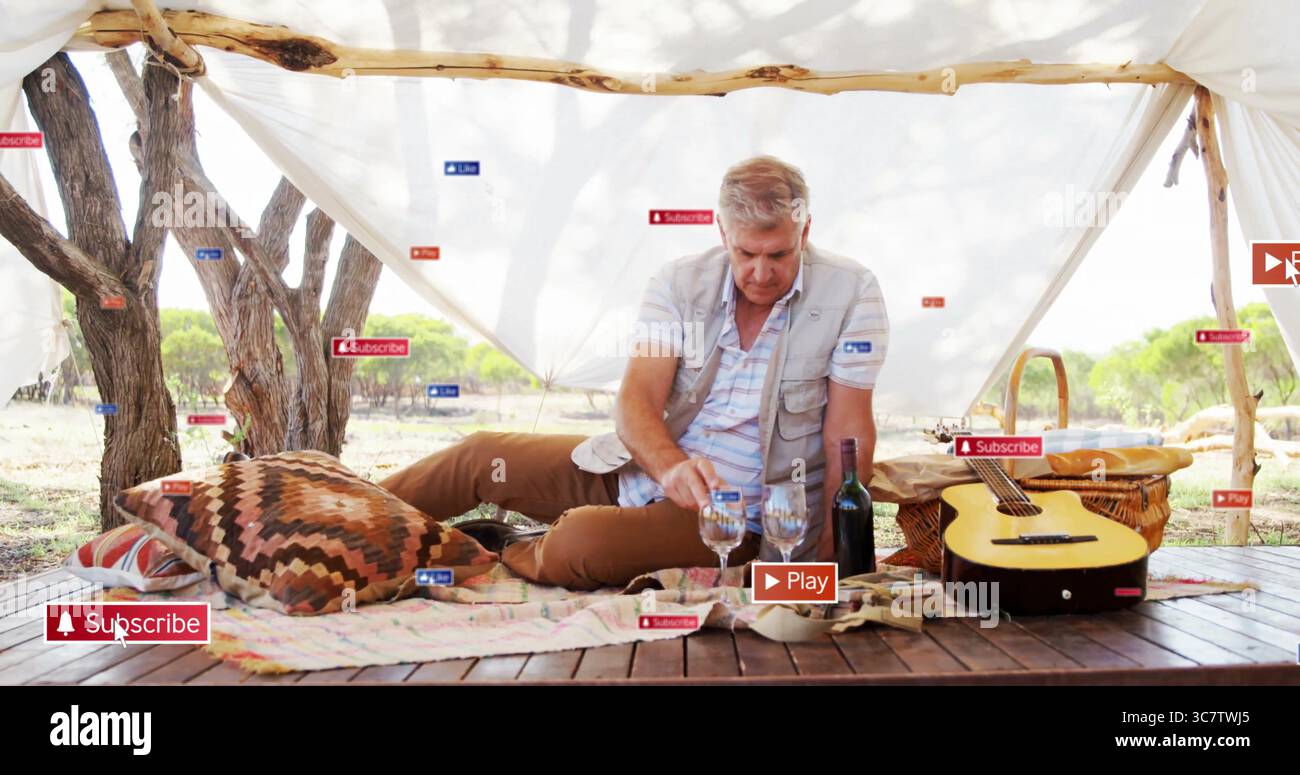 Liegender, erwachsener Mann, der drei Weingläser unter weißem Vordach auf hölzerner Plattform mit Gitarre anfasst Stockfoto