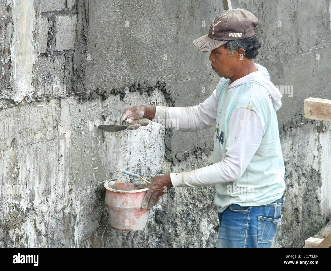 Badung, Bali, Indonesien – 1. August 2025: Bauarbeiter, die mit einer Kelle und einem Mischmörtel Zementputz auf eine Betonwand aufbringen Stockfoto
