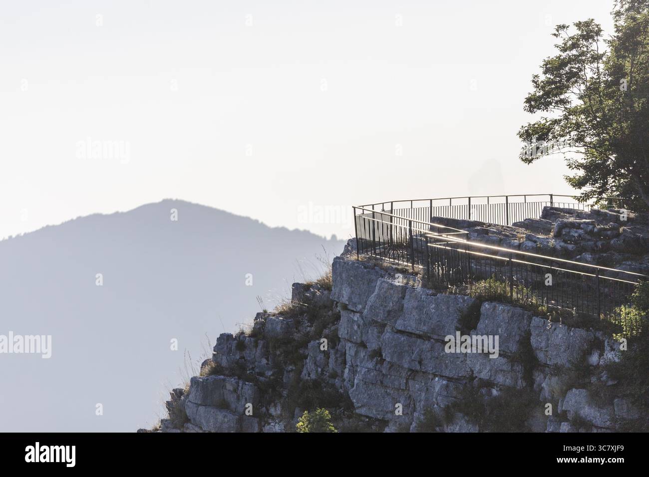 Blick auf einen Abgrund mit einer Sicherheitsgeländer, wo die Felsstrukturen auf den hellen Himmel treffen, im Kontrast zu einem fernen Berg, Avellino, Kampanien, Italien. Stockfoto