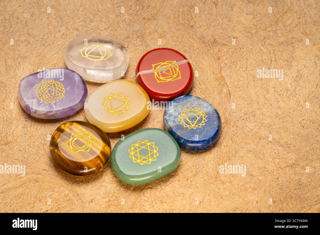 Sieben Chakra-Steine mit Symbolgravur auf strukturiertem, handgefertigtem Rindenpapier, reiki-Heilungskonzept Stockfoto