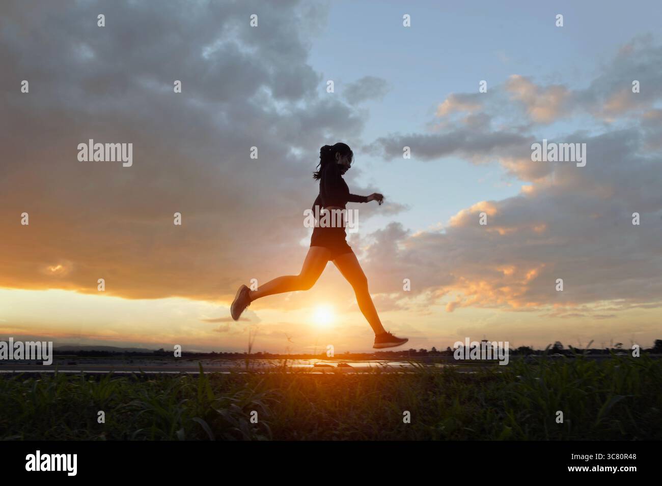 Seitenansicht einer jungen Frau, die bei Sonnenuntergang durch eine ländliche Landschaft joggt, Thailand Stockfoto