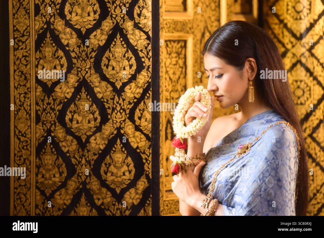 Nahaufnahme einer jungen Frau in traditioneller thailändischer Kleidung, die eine Blumengirlande riecht (Phuang Malai) Stockfoto