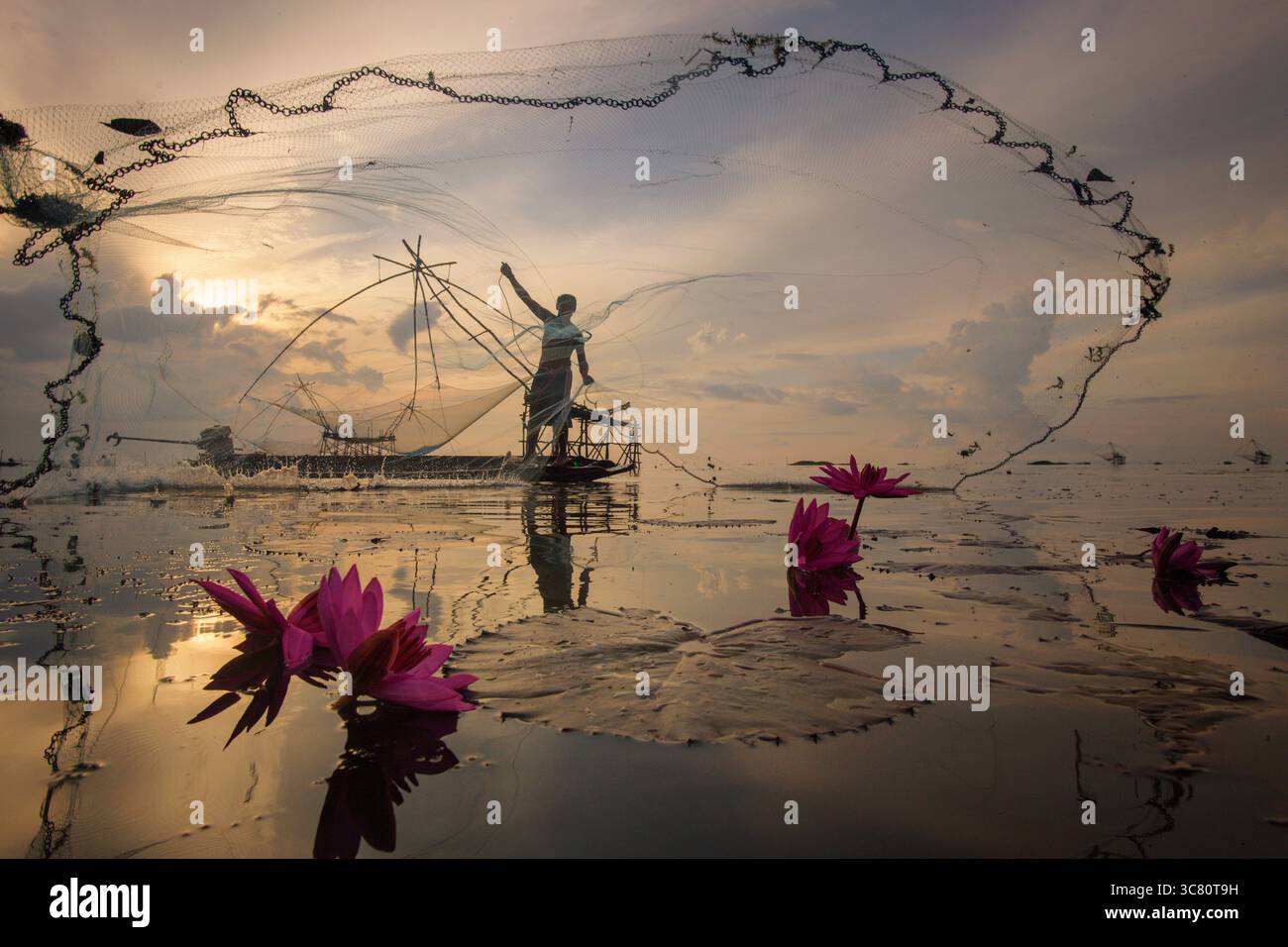Silhouette eines Fischers, der bei Sonnenaufgang auf einem Boot steht und sein Fischernetz wirft, am Bang Phra Reservoir (Bangpra Lake), Chon Buri, Thailand Stockfoto