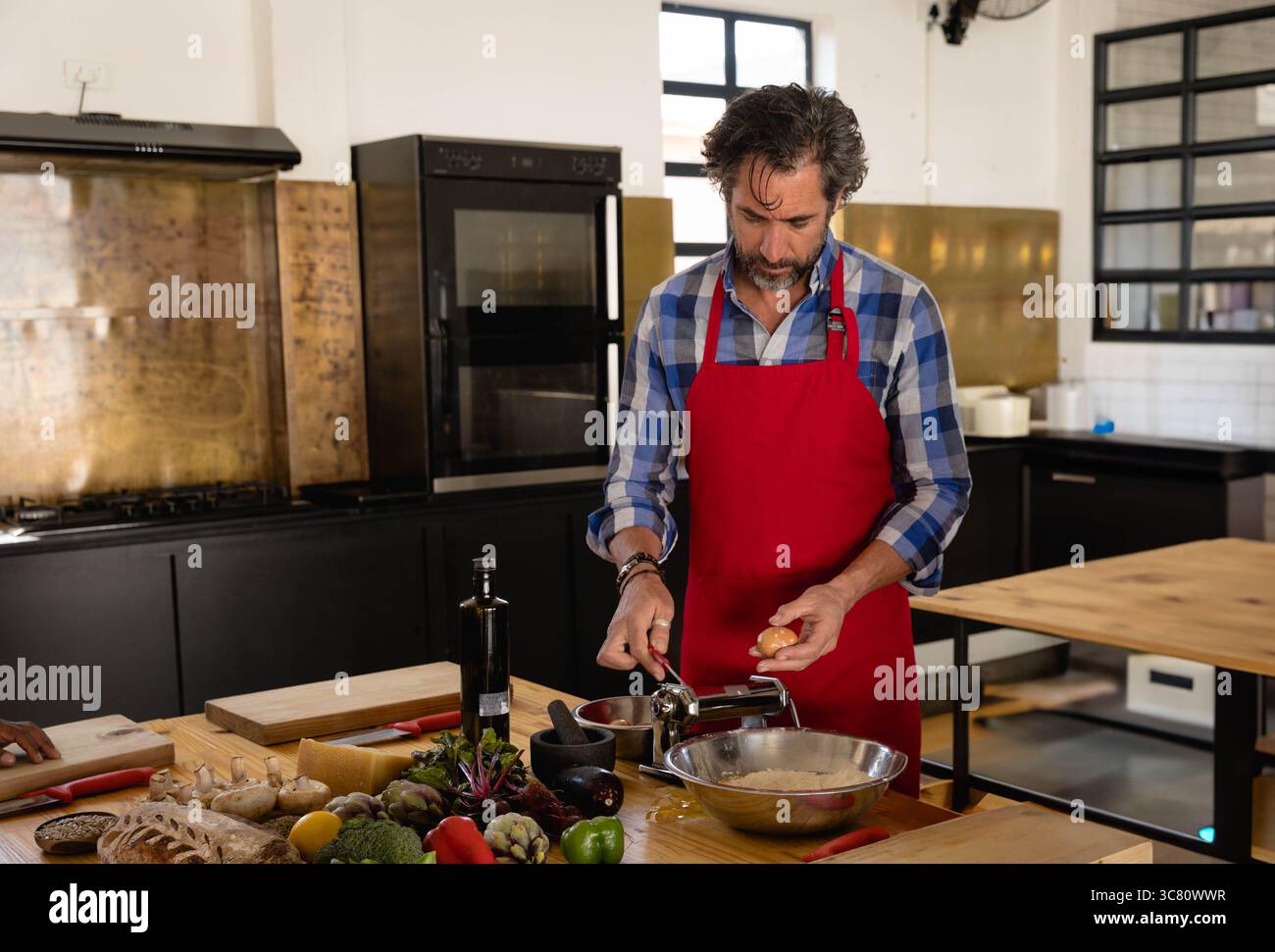 In der Küche kochen die mittleren Alters, knacken Eier und drehen Nudelteig mit der Handkurbel auf dem Vorbereitungstisch Stockfoto