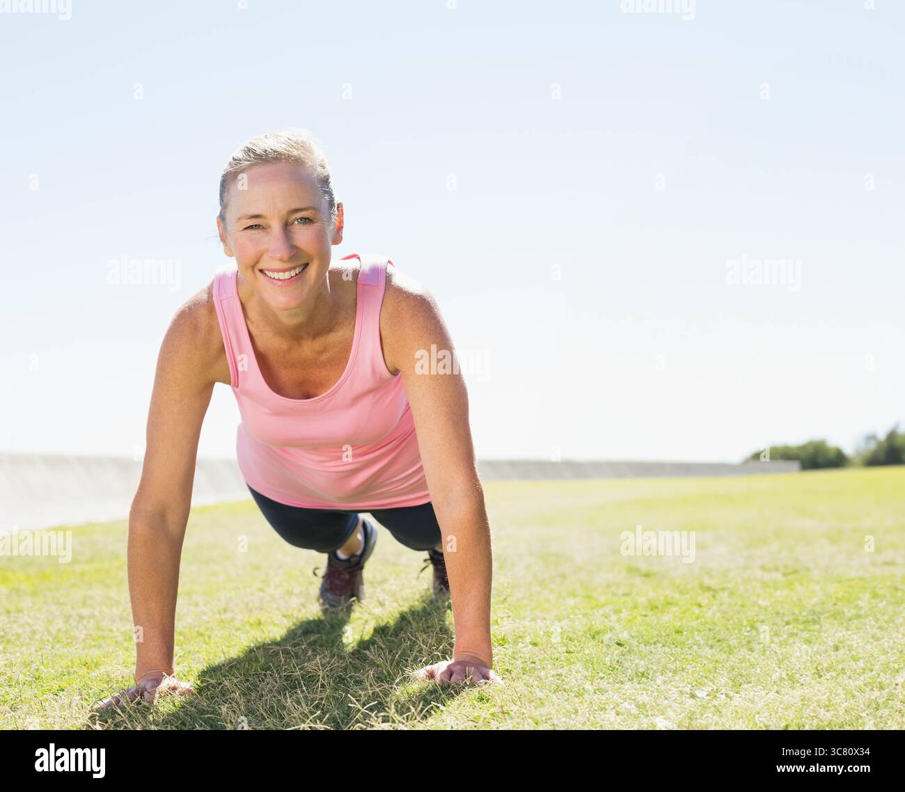 Reife Erwachsene Frau mit Planke auf dem Grasfeld im Park, die sportliche Schuhe und Leggings zeigt Stockfoto