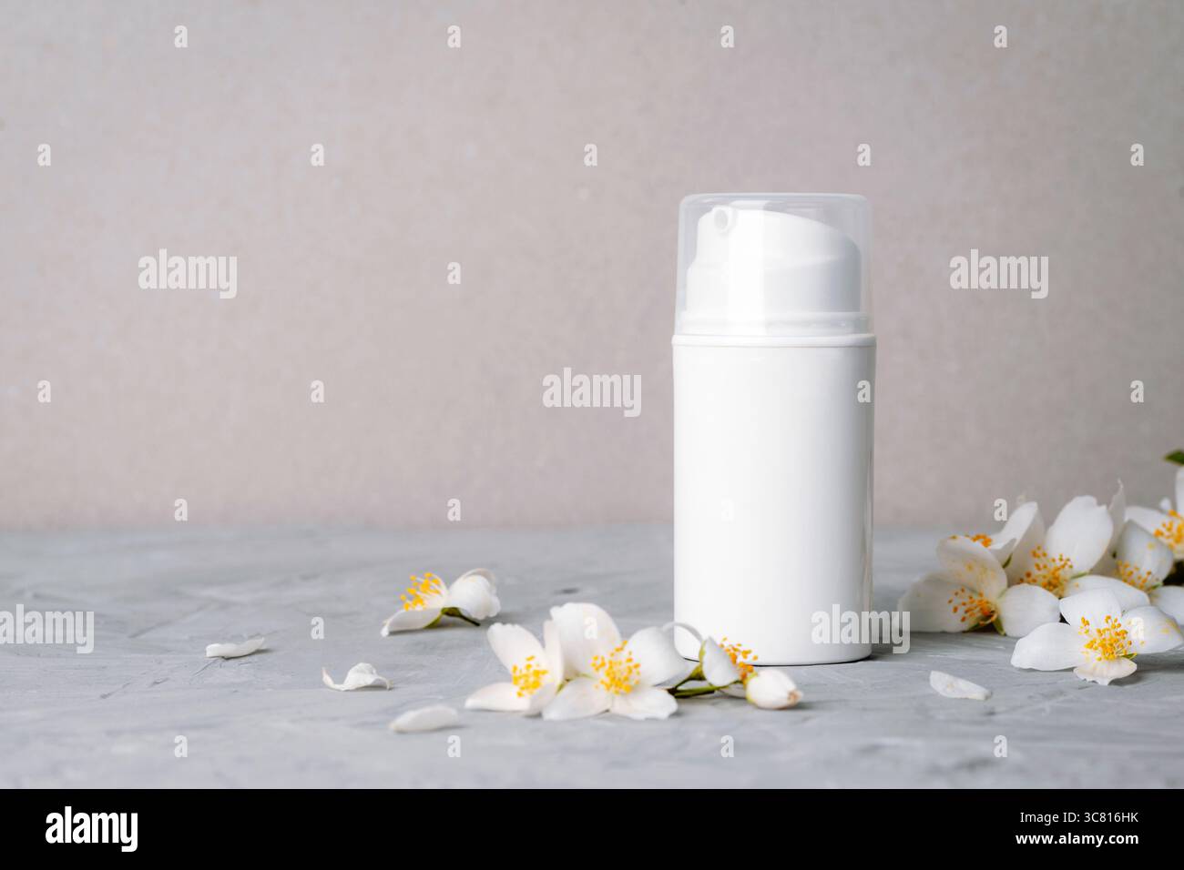 Weiße Kosmetikflasche und Jasminblüten auf grauem Hintergrund. Naturkosmetik, Spa- und Wellnesskonzept. Kopierbereich. Stockfoto