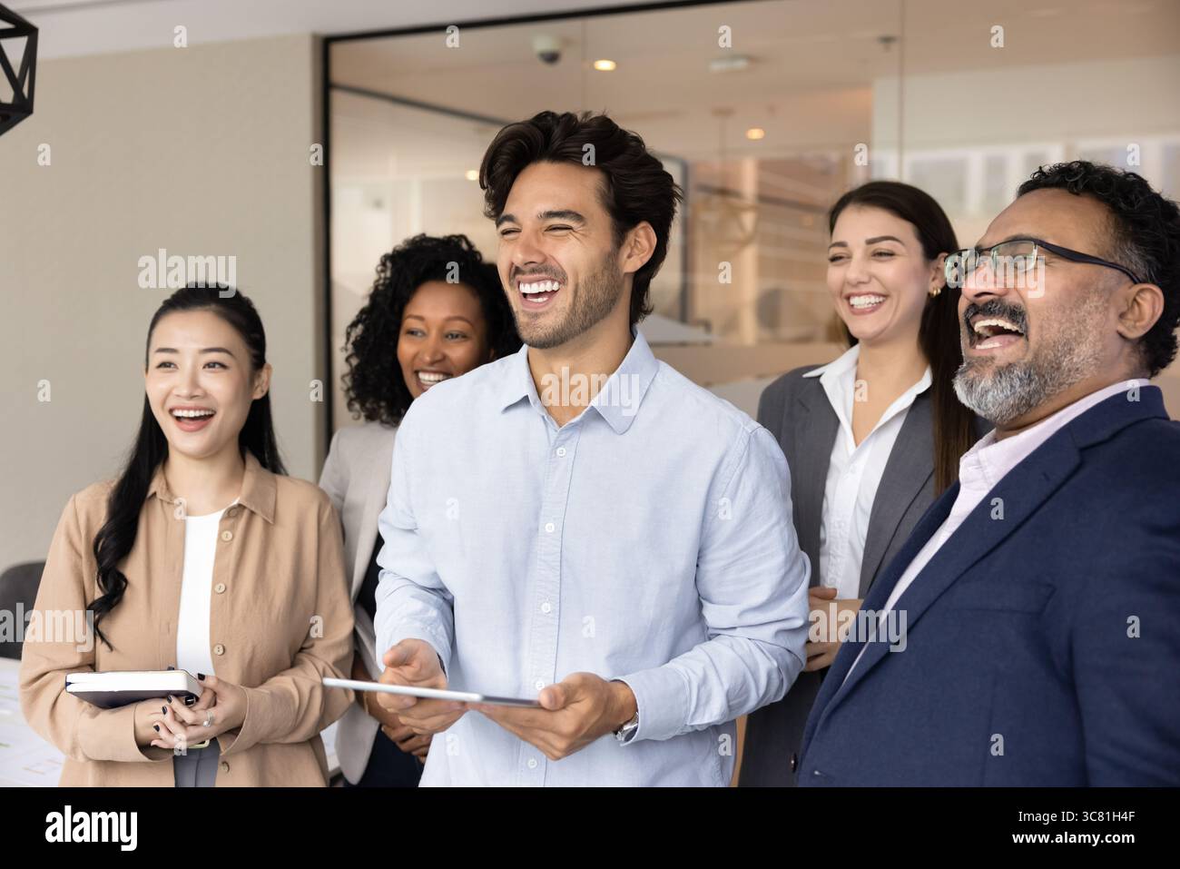Glückliche, freundliche internationale Geschäftsleute, die gemeinsam am Arbeitsplatz stehen Stockfoto