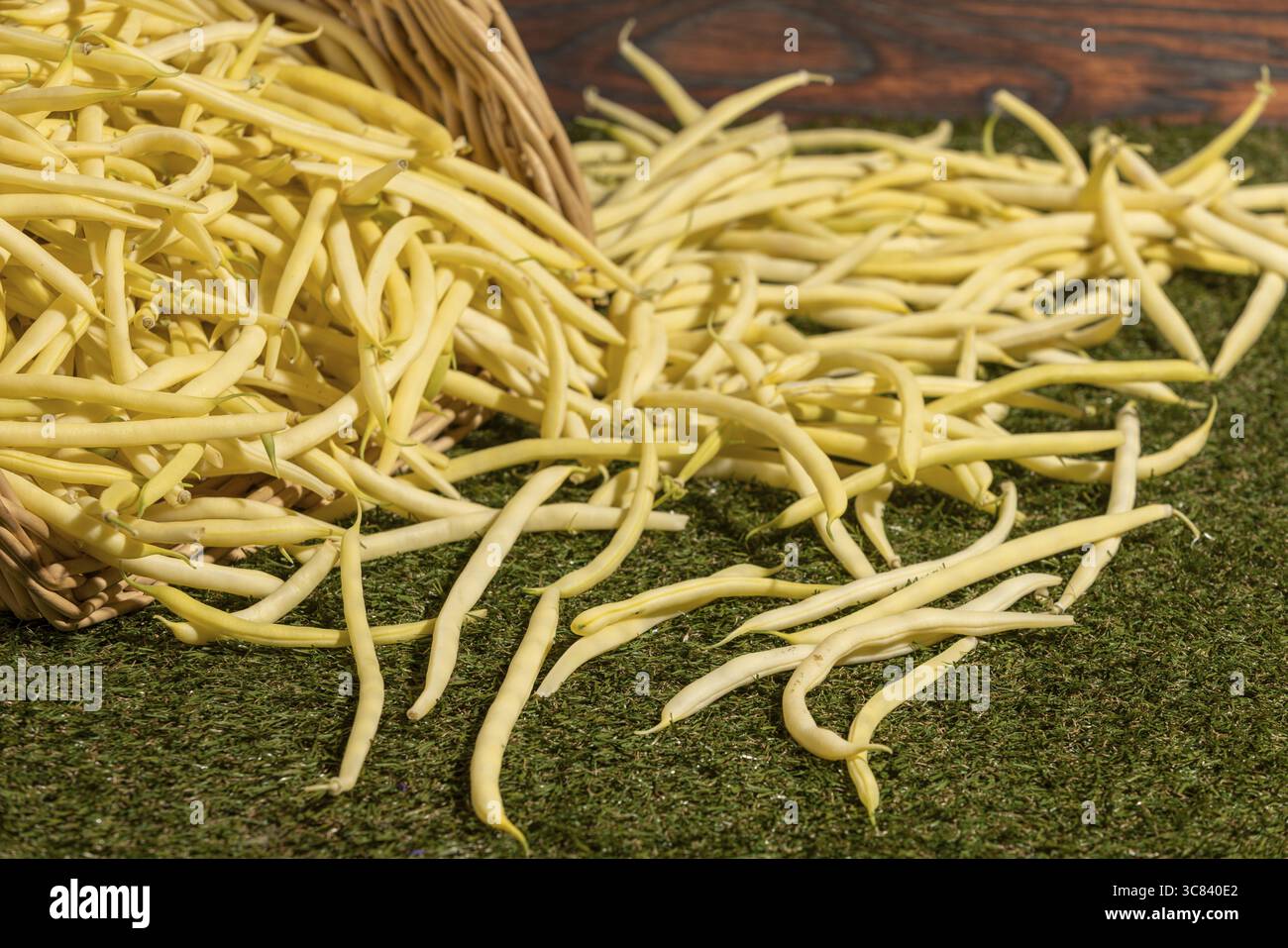 Gelbe Bohnen über Gras verteilt, umgekippter Korb Stockfoto