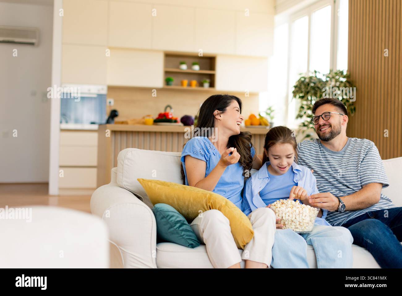 In einem warmen und einladenden Wohnzimmer teilt sich eine Familie eine Schüssel Popcorn, während sie zusammen in einem Film eine gute Zeit genießt. Stockfoto