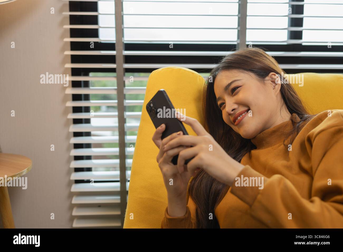 Lächelnde junge Frau zu Hause mit modernem Smartphone, Online-Chat, schöne Frau, die sich zu Hause entspannt und Musik hört und andere Dinge, die sie mag, pe Stockfoto