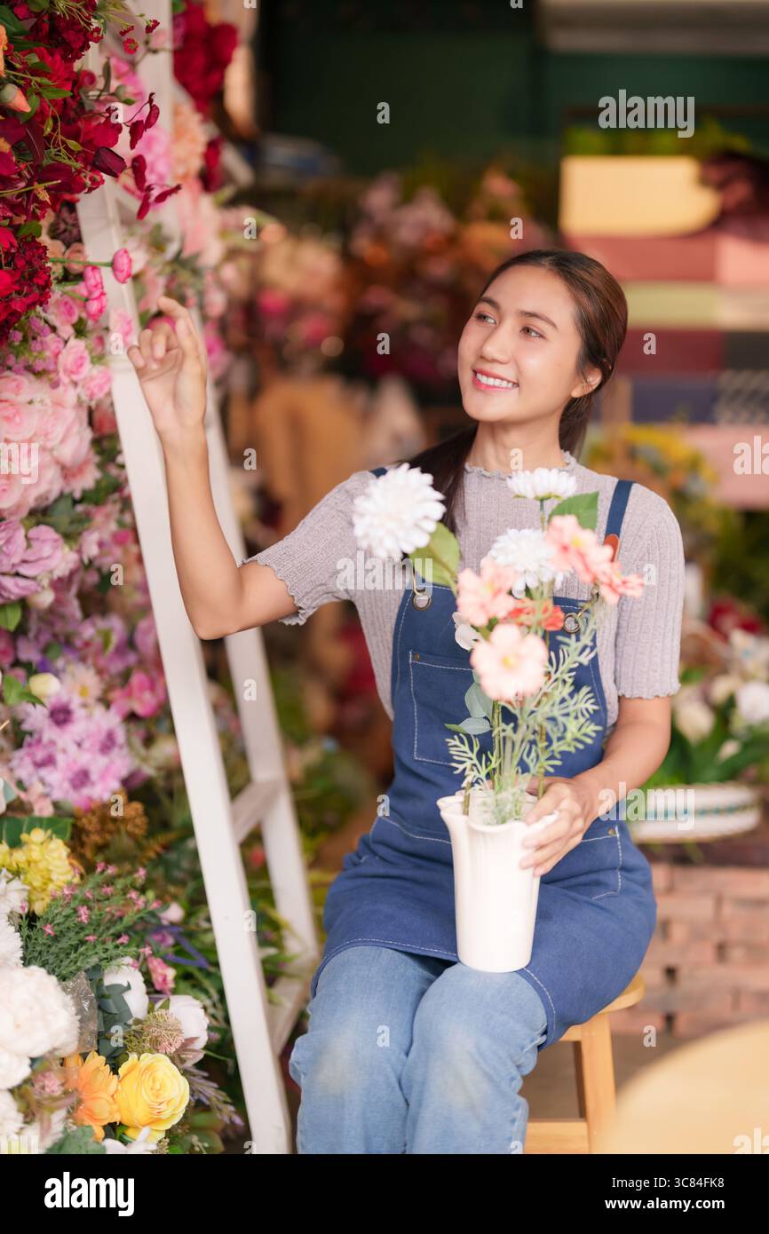 Glückliche junge asiatische Floristin kuratiert schöne Blüten Sie arrangiert frische Blumen, um bezaubernde Ladenpräsentationen und eine herrliche Kundenerfahrung zu schaffen Stockfoto