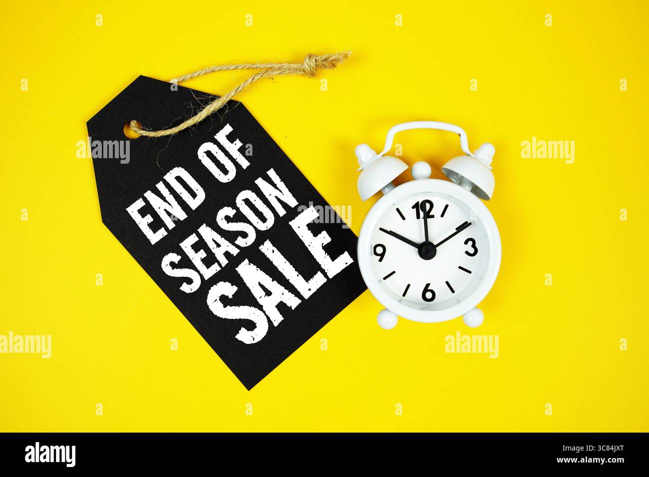 Verkaufstext am Ende der Saison auf dem Preisschild mit Wecker auf gelbem Hintergrund Stockfoto