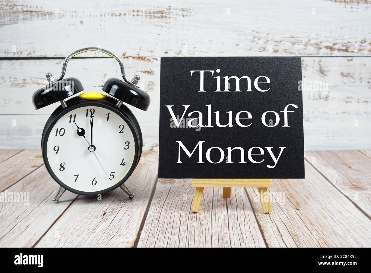 Zeitwert des Geldtextes mit Staffelei und Wecker auf hölzernem Hintergrund Stockfoto