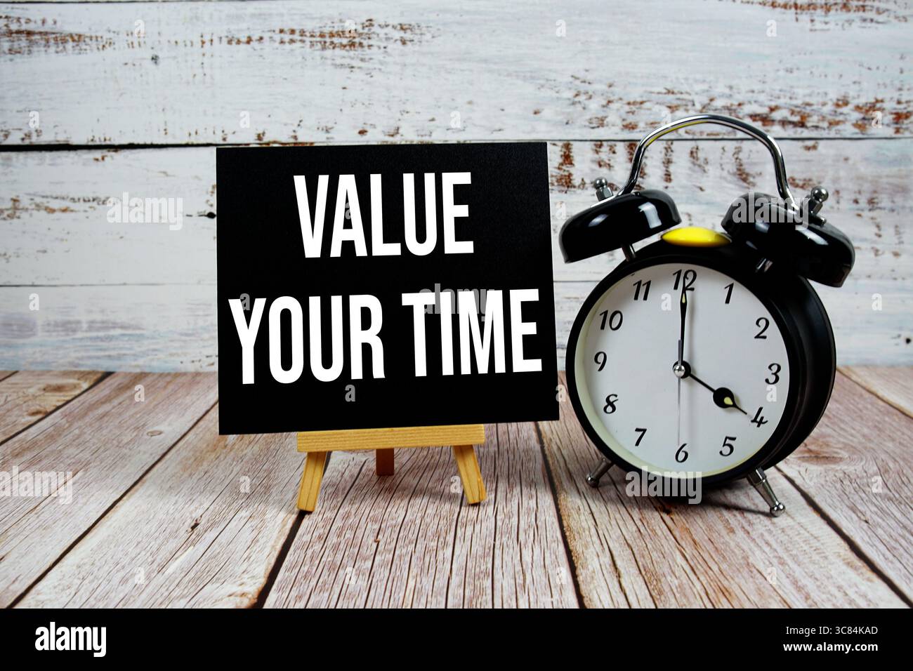 Schätzen Sie Ihren Zeittext mit Staffelei und Wecker auf hölzernem Hintergrund Stockfoto