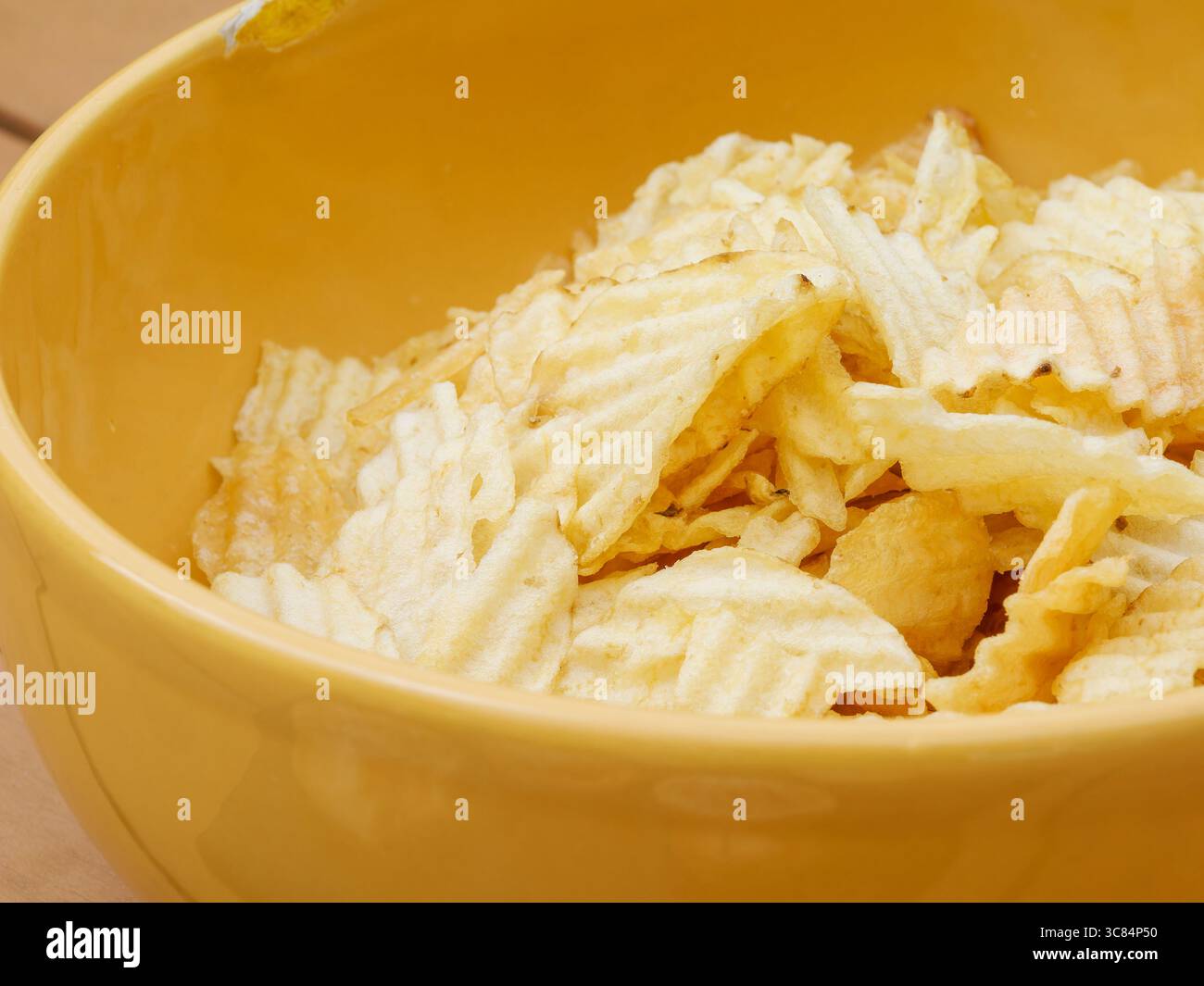 Knackgeschnittene Kartoffelchips in einer leuchtend gelben Schüssel, die während einer goldenen Hochzeitsfeier im Freien in entspannter und festlicher Atmosphäre festgehalten werden Stockfoto