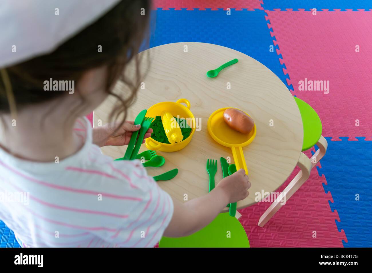 Kind, das mit grünen Spielutensilien und Lebensmitteln auf einem kleinen runden Holztisch spielt, Konzept der Lernspiele, frühkindliche Erziehung, Spielwarengeschäfte Stockfoto