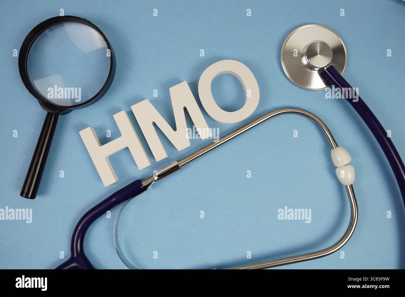 HMO-Abkürzung für Buchstaben der Gesundheitsorganisation mit Vergrößerungsglas und Stethoskop auf blauem Hintergrund Stockfoto
