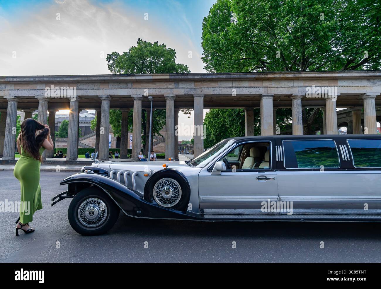 Stilvolle Frau in grünem Kleid posiert im Sommer in der Alten Nationalgalerie in der klassischen Stretchlimousine vor historischen Kolonnaden. Stockfoto