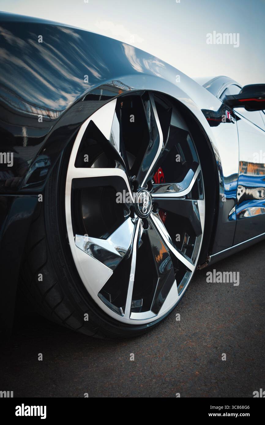 Alufelge aus einem Audi Auto mit eckigem zweifarbigem Diamantdesign, sichtbarem rotem Bremssattel und flachem Reifen. Stockfoto