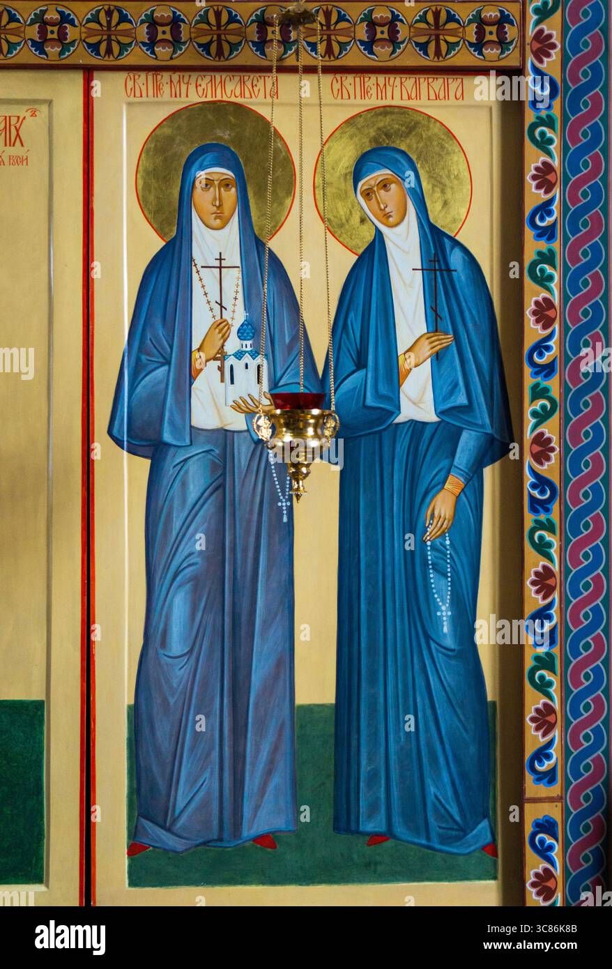 Zwei weibliche Heilige stehen nebeneinander, in fließenden blauen Gewändern gekleidet. Sie tragen Symbole ihres Glaubens, beleuchtet durch Kerzenlicht in einer ruhigen Kirche Stockfoto