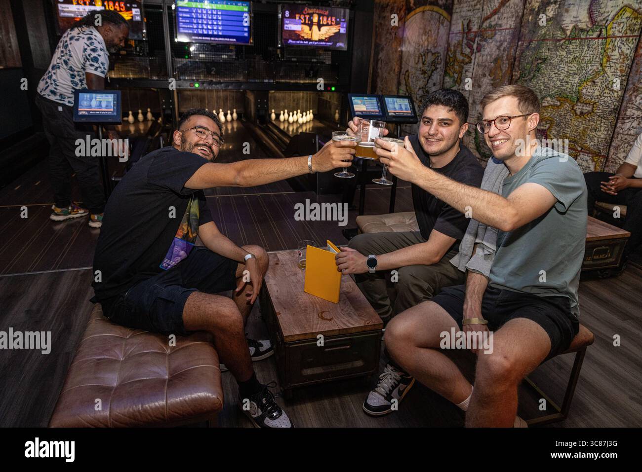 Gruppe junger Männer, die in einer Bowlingbahn Biergläser anstoßen, feiern und einen Abend mit Getränken, Spaß und Kameradschaft genießen. Stockfoto