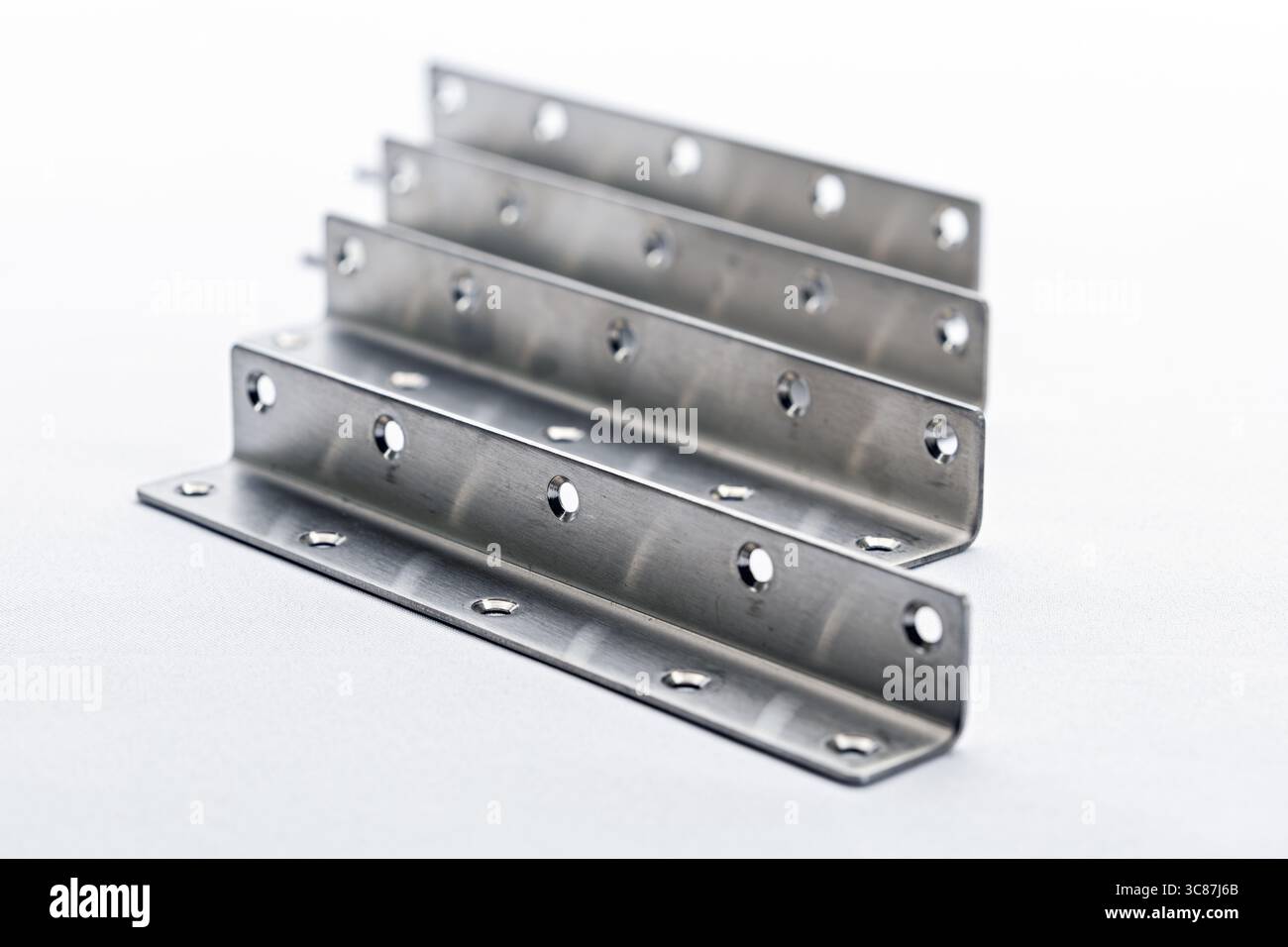 Die Winkelhalterungen aus Edelstahl mit Bohrungen sind in Reihe angeordnet, um ihre metallische Oberfläche und ihre Präzisionstechnik zu demonstrieren. Diese Halterungen sind ideal Stockfoto