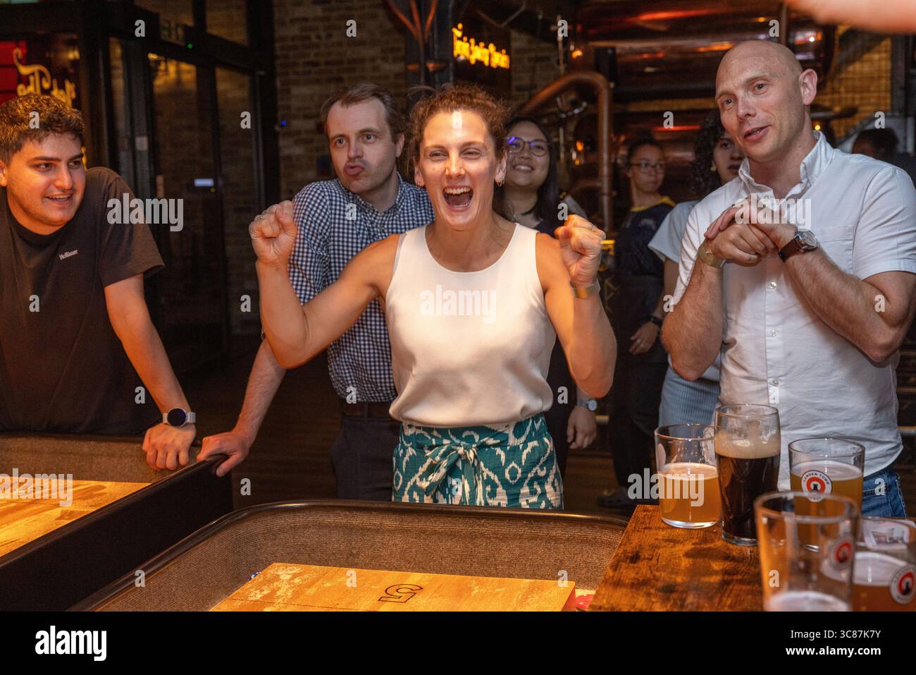 Junge Freunde, die ein Shuffleboard-Spiel gewinnen , zeigen Spannung und Kameradschaft während eines lustigen Abends in der Bar . Stockfoto
