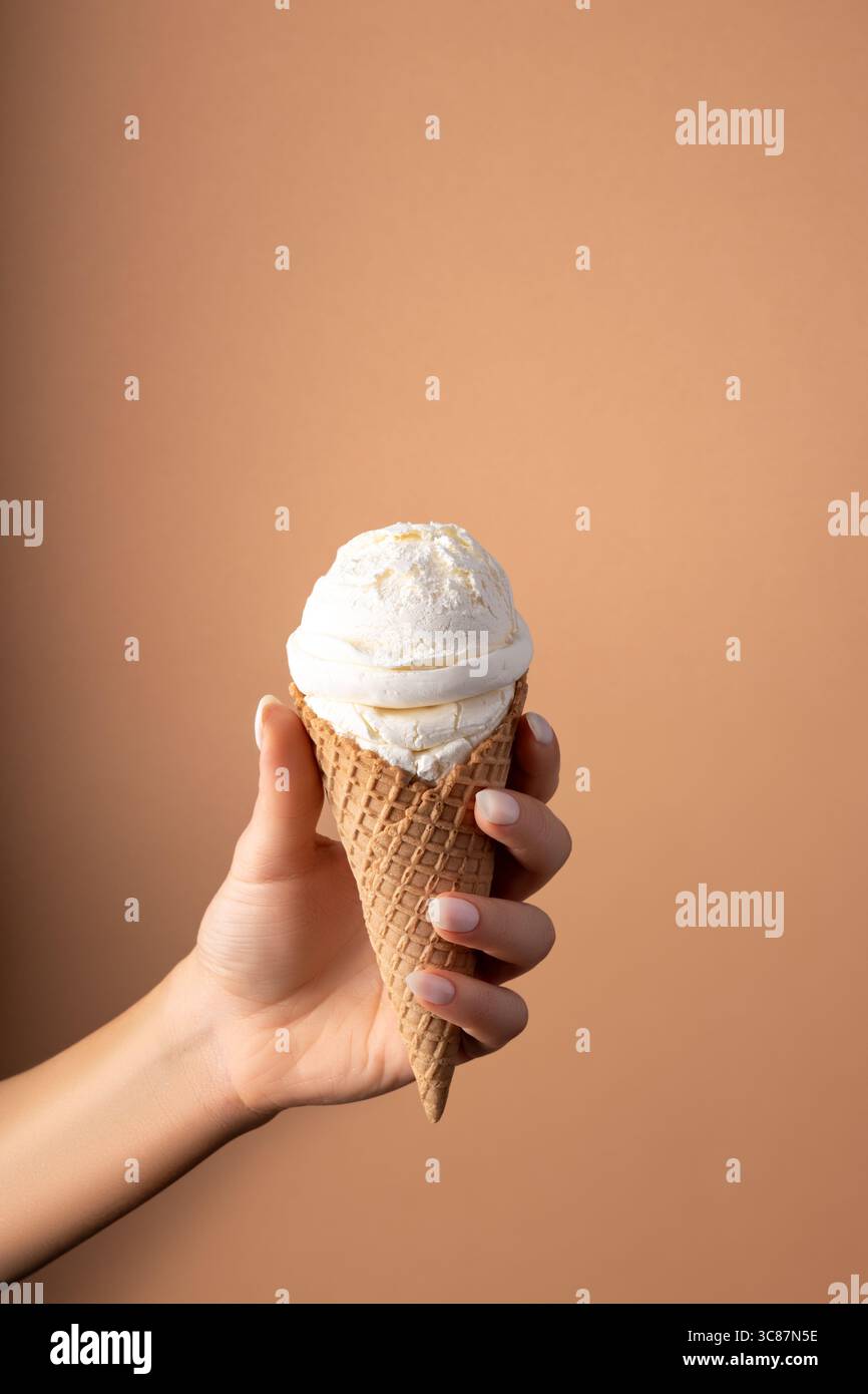 Weißer Eislöffel mit Eiskegel in der Hand auf hellem Hintergrund. Minimales Sommerkonzept. Stockfoto