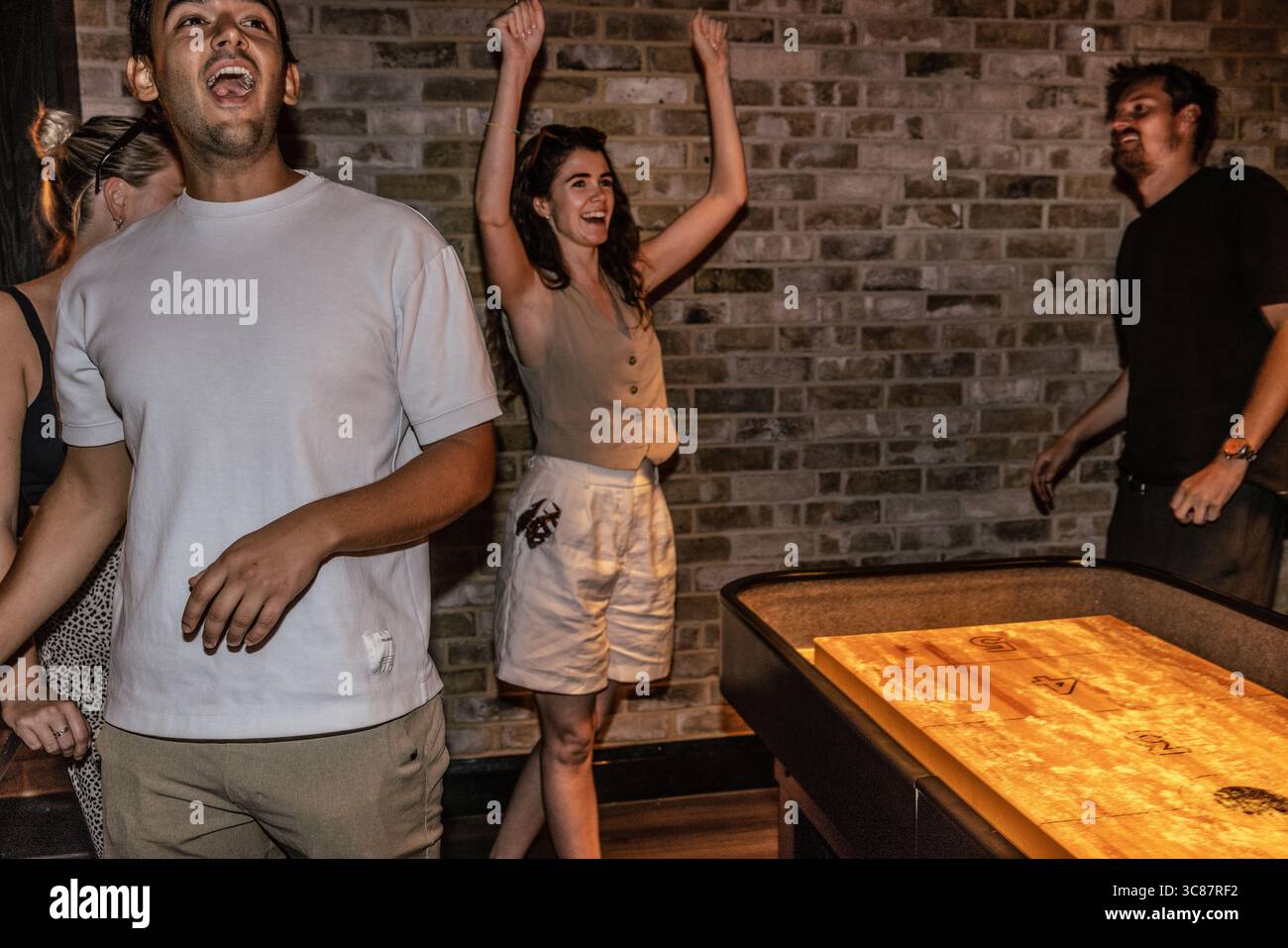 Junge Freunde, die ein Shuffleboard-Spiel gewinnen, zeigen Spannung und Kameradschaft während eines lustigen Abends in einer Bar. Stockfoto