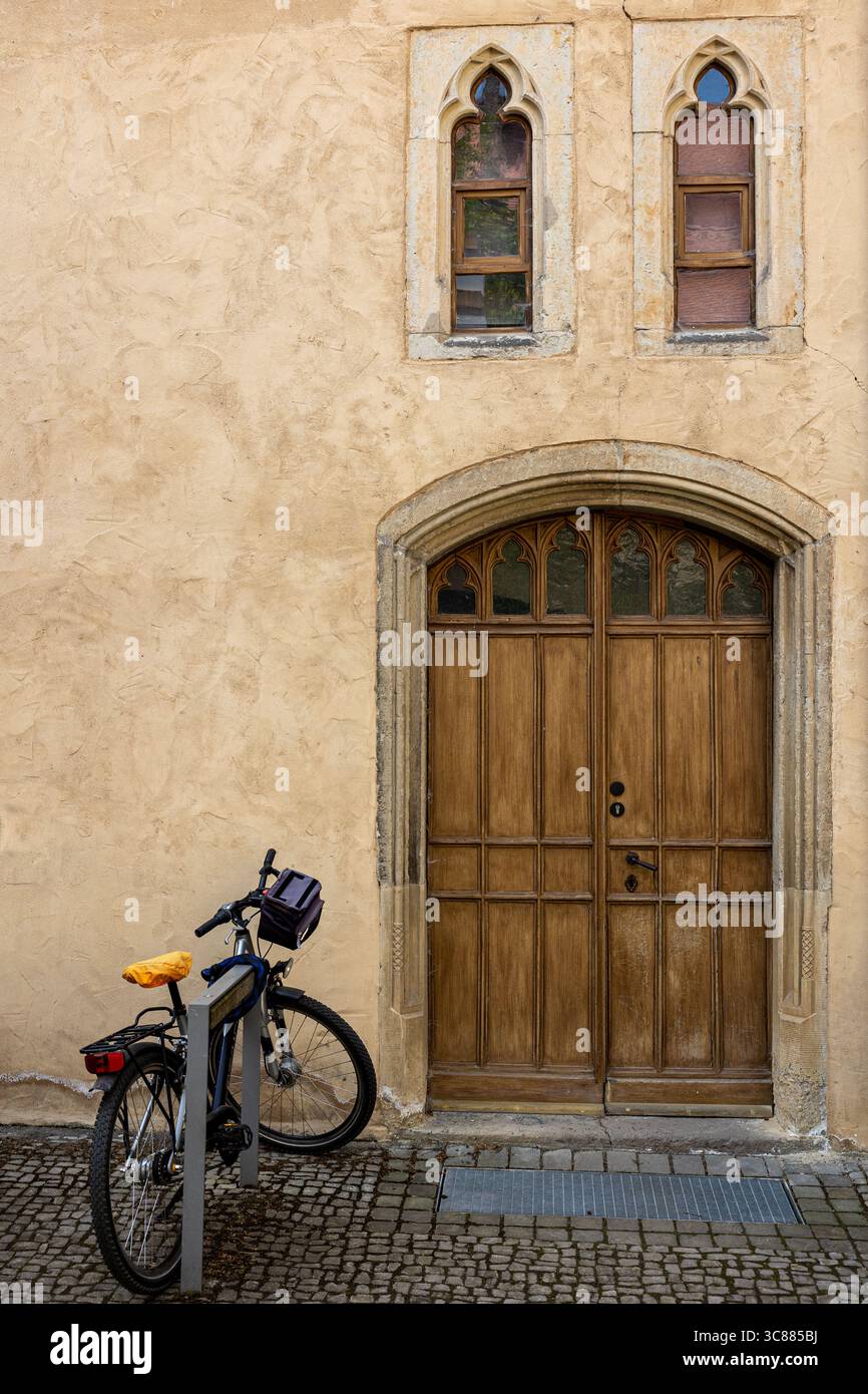Stillleben zeigt ein modernes Fahrrad, das vor einem mittelalterlichen Gebäude mit einzigartigen Fenstern und einer doppelten Holztür in Deutschland geparkt ist. Stockfoto
