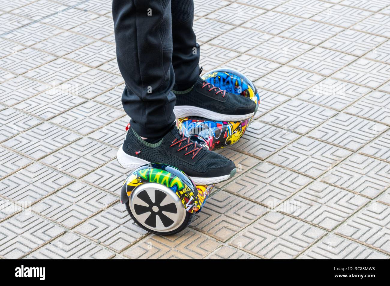 Junge in schwarzen Turnschuhen, der auf dem Hoverboard auf der Backsteinstraße fährt. Neue Technologien. Selbstausbalancierendes elektrisches Smart Skateboard. Elektroroller zum Spielen Stockfoto