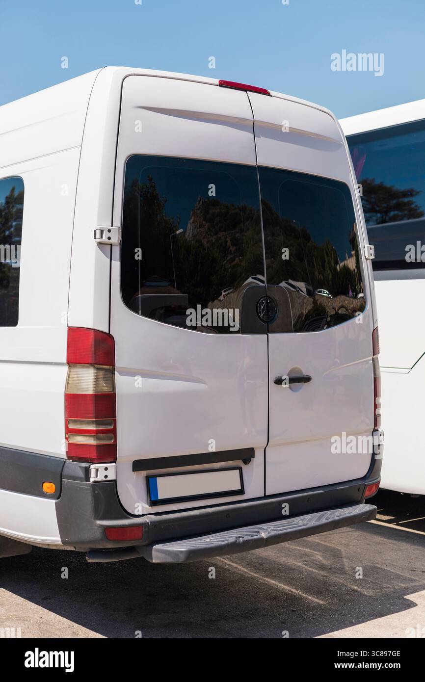 Ein großer weißer Van mit getönten Fenstern steht in einem Transportbereich neben einem anderen Fahrzeug. Der klare blaue Himmel verstärkt den Fokus auf die beiden Fahrzeuge Stockfoto