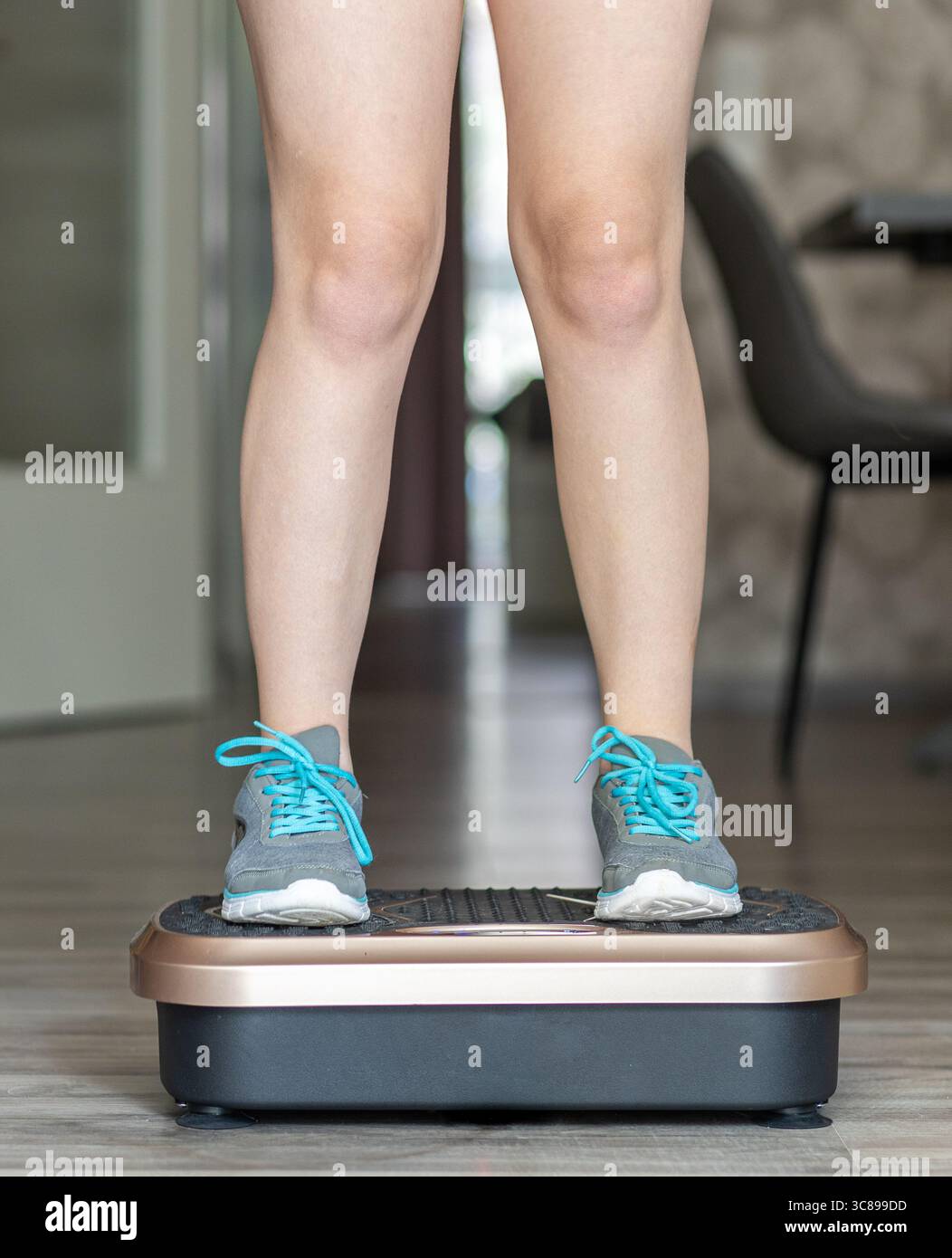 Die Person steht auf einer Vibrationsplattform in einem modernen Raum und demonstriert Fitness-Übungen, mit stilvollem Dekor und Bodenbelag, die Wellness A hervorheben Stockfoto
