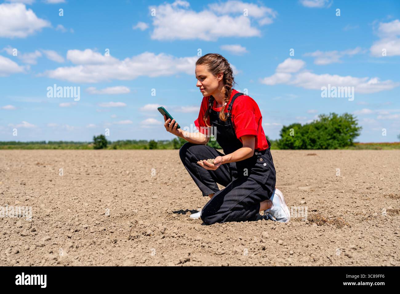 Agrarwissenschaftlerin mit Smartphone zur Bodenbeurteilung vor Düngemittelausbringung in der modernen nachhaltigen Landwirtschaft Stockfoto