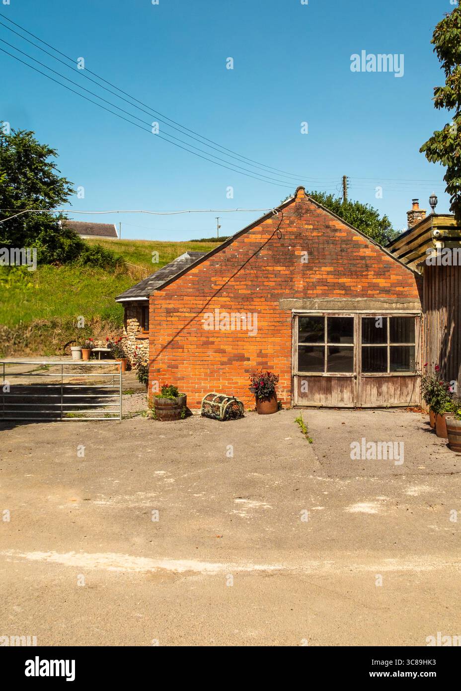 Ein Backsteingebäude mit einer Holztür und einem klaren blauen Himmel im Hintergrund. Vor dem Gebäude befinden sich Topfpflanzen und eine Hummerfalle. Stockfoto