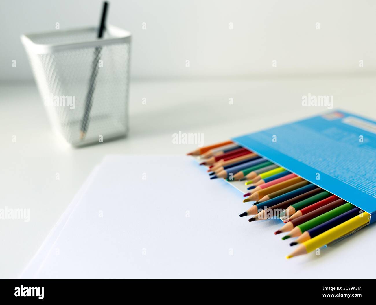 Weißer Schreibtisch mit Ständer mit farbigen Bleistiften und Skizzenbuch. Schulutensilien auf dem Tisch, wunderschön beleuchtet durch eine Schreibtischlampe Stockfoto