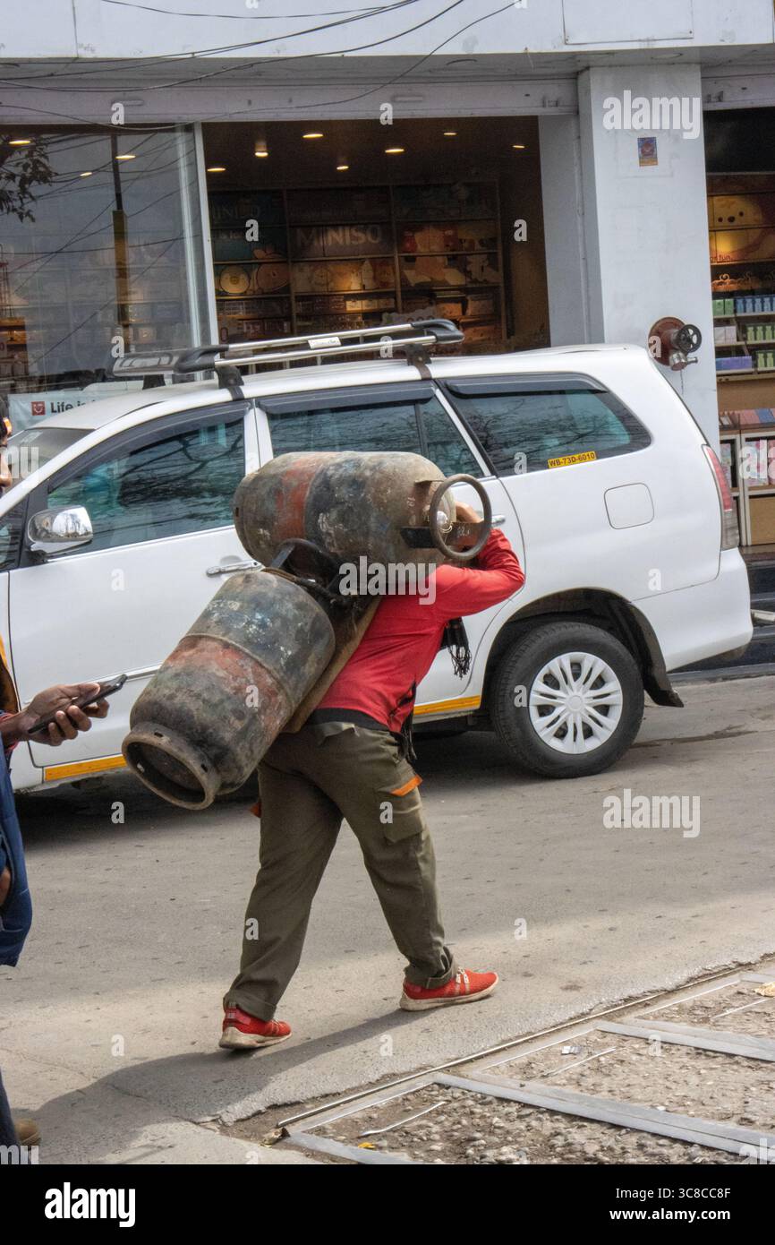 DARJEELING, WESTBENGALEN, INDIEN - 8. FEBRUAR 2024 typischer Mann mit zwei Treibgastanks auf dem Rücken den Hügel hinauf Stockfoto