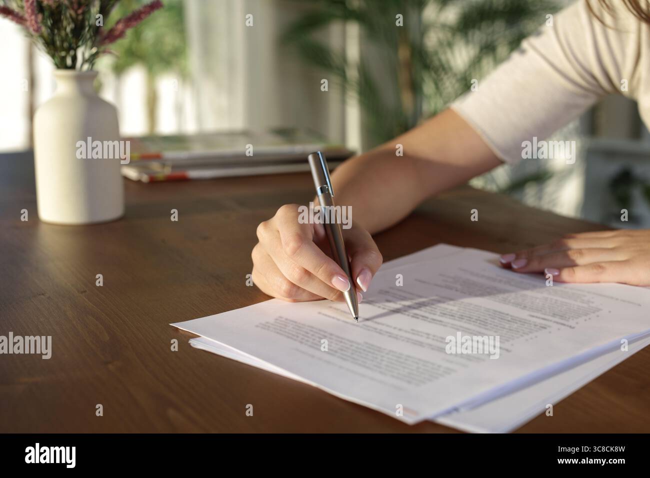 Clos eup einer Frau, die zu Hause Dokumente auf einem Holztisch ausfüllt Stockfoto