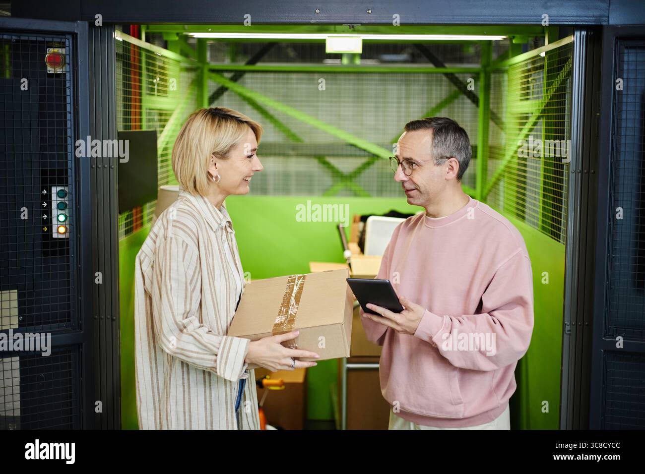 Kaukasische Frau mittleren Alters übergibt Parcel an einen kaukasischen Mann mittleren Alters lächelnd Stockfoto