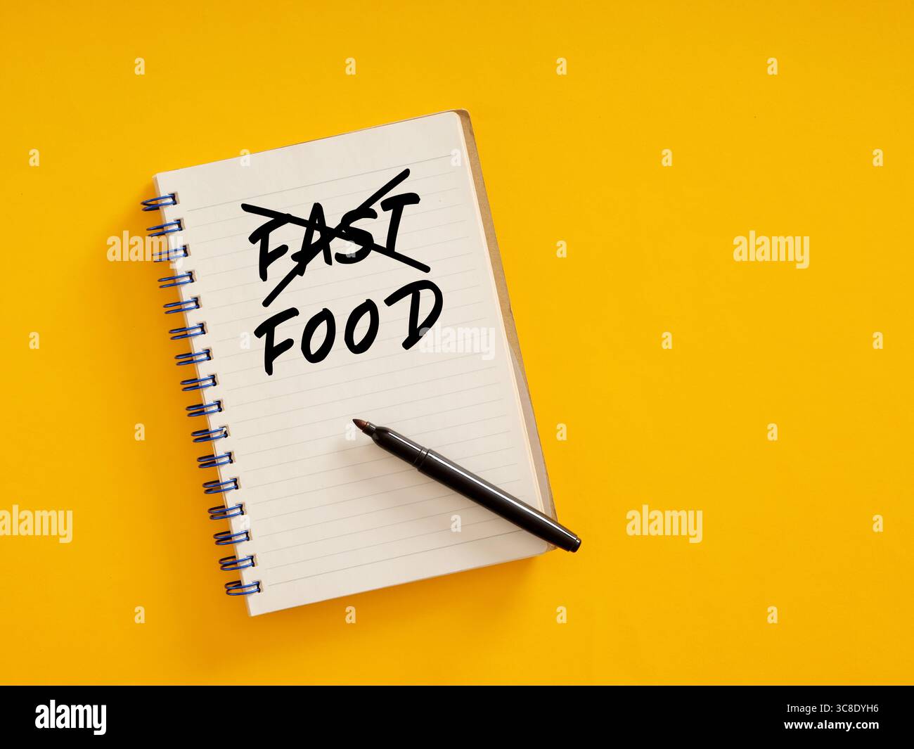 Notizblock mit durchgestrichener Fast-Food-Schrift und Stift auf gelbem Hintergrund steht für die Ablehnung ungesunder Essgewohnheiten Stockfoto