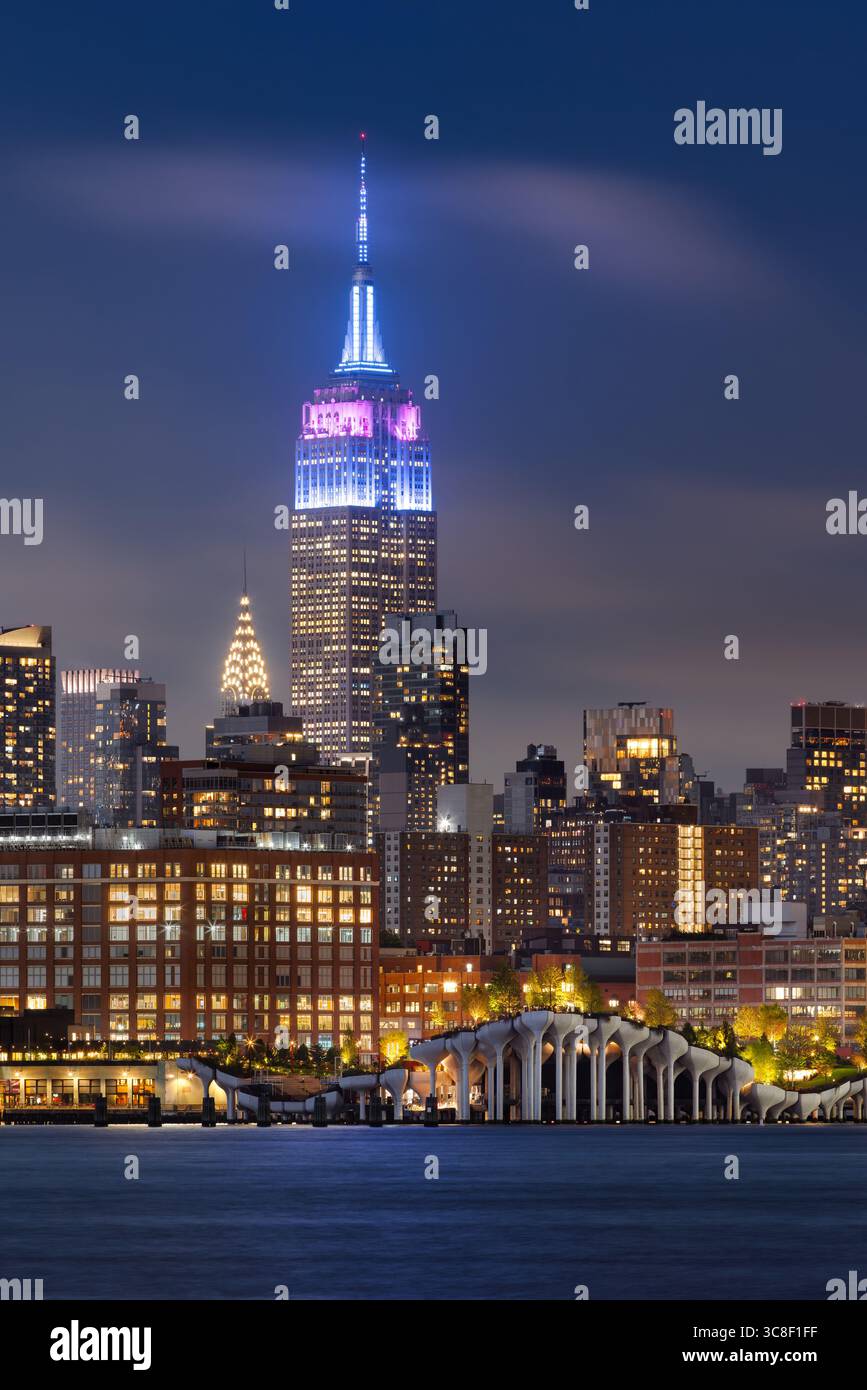 Empire State Building in Blau und Lila in der Abenddämmerung. Blick über Little Island und die Skyline von Midtown Manhattan vom Hudson River aus. New York City Stockfoto
