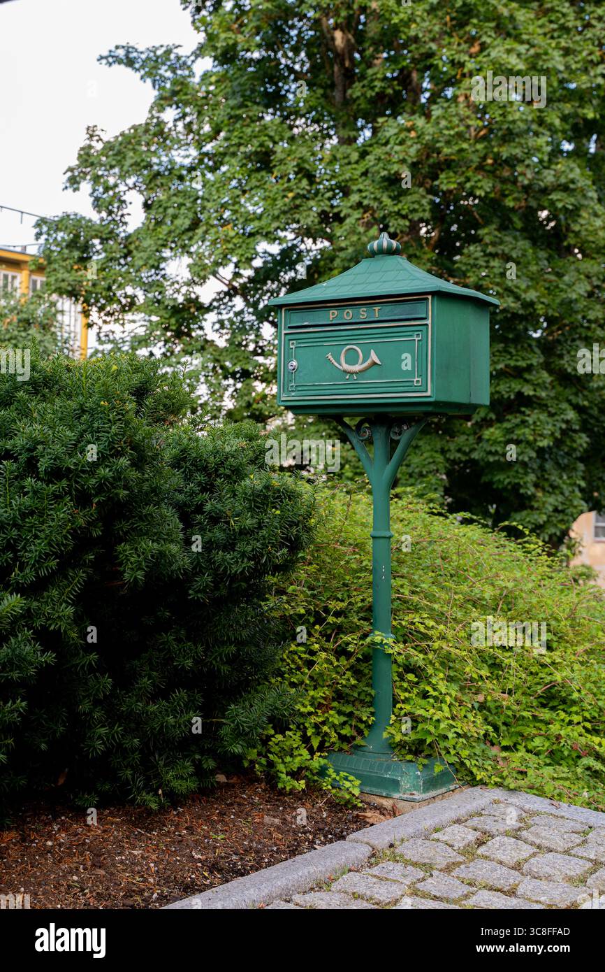Grüner Briefkasten im Vintage-Stil auf einer Post in Viljandi, Estland, dekorativer öffentlicher Briefkasten mit Hornemblem in einer landschaftlich gestalteten städtischen Umgebung Stockfoto
