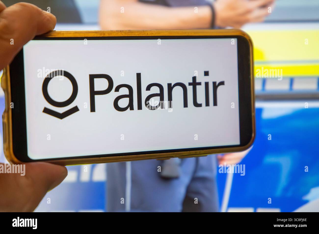 Fotomontage PALANTIR Symbolbild: Logo von PALANTIR auf einem Smartphone, im Hintergrund ein Polizist *** Fotomontage PALANTIR Symbolbild PALANTIR Logo auf einem Smartphone, ein Polizeibeamter im Hintergrund Copyright: XUdoxHerrmannx Stockfoto